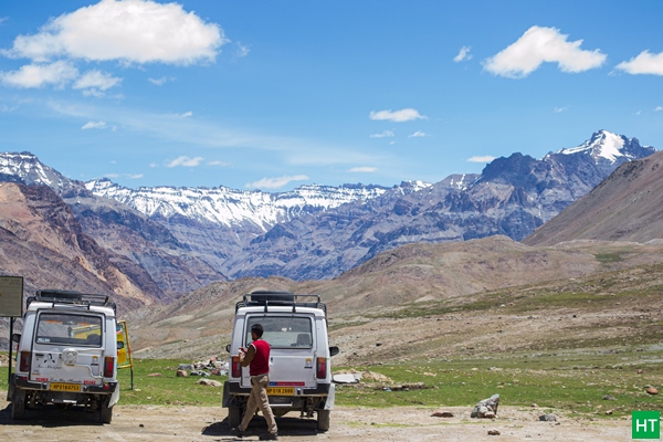 Road‑trip pause near Kunzum La with SUVs parked and Spiti’s snow‑lined ranges ahead — fast coverage