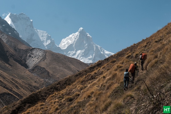 Trekking group ascending grassy slope towards Kedartal with Thalay Sagar and snow peaks in view.