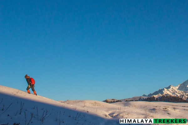 Trekker wearing red gaiters walking on compacted snow, Indian Himalayan winter trail.